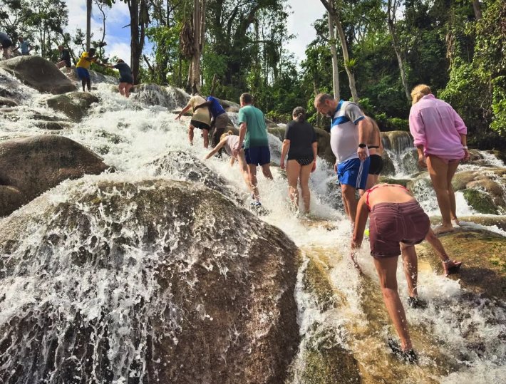 Visitors climbing the falls in a linked chain on a trip from Montego Bay